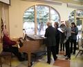 Members gather together and sing Christmas carols, with Paul Engel accompanying them on the piano.