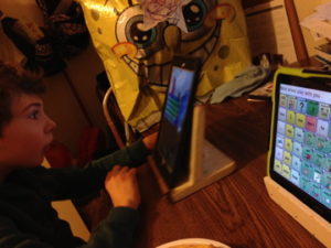 Bolin's son, Finnegan, plays Wheel of Fortune on his iPad while a SpongeBob balloon looms in the background. His communication device screen reads 